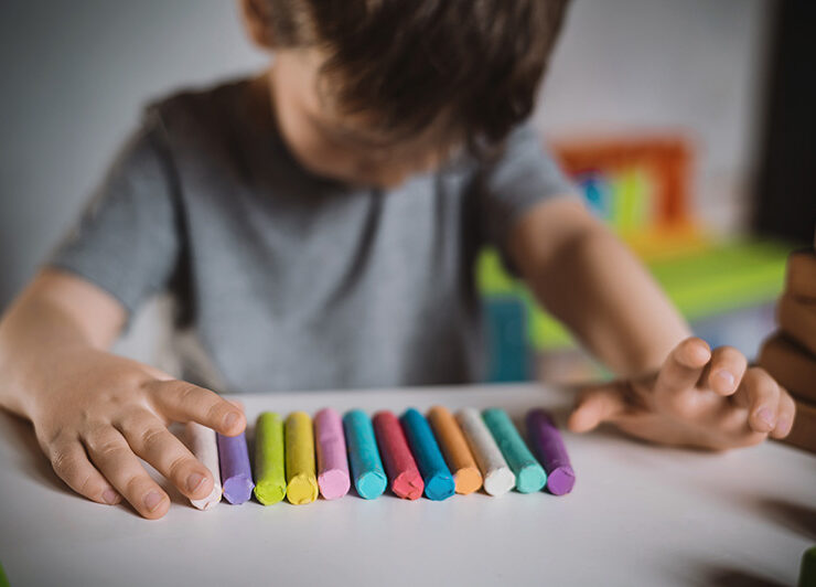 A boy with autism looks down while playing with clay during a therapy session.