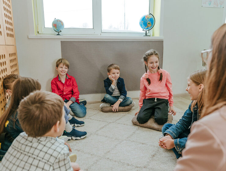 Children sit in a circle and participate in group therapy under the supervision of a therapist.